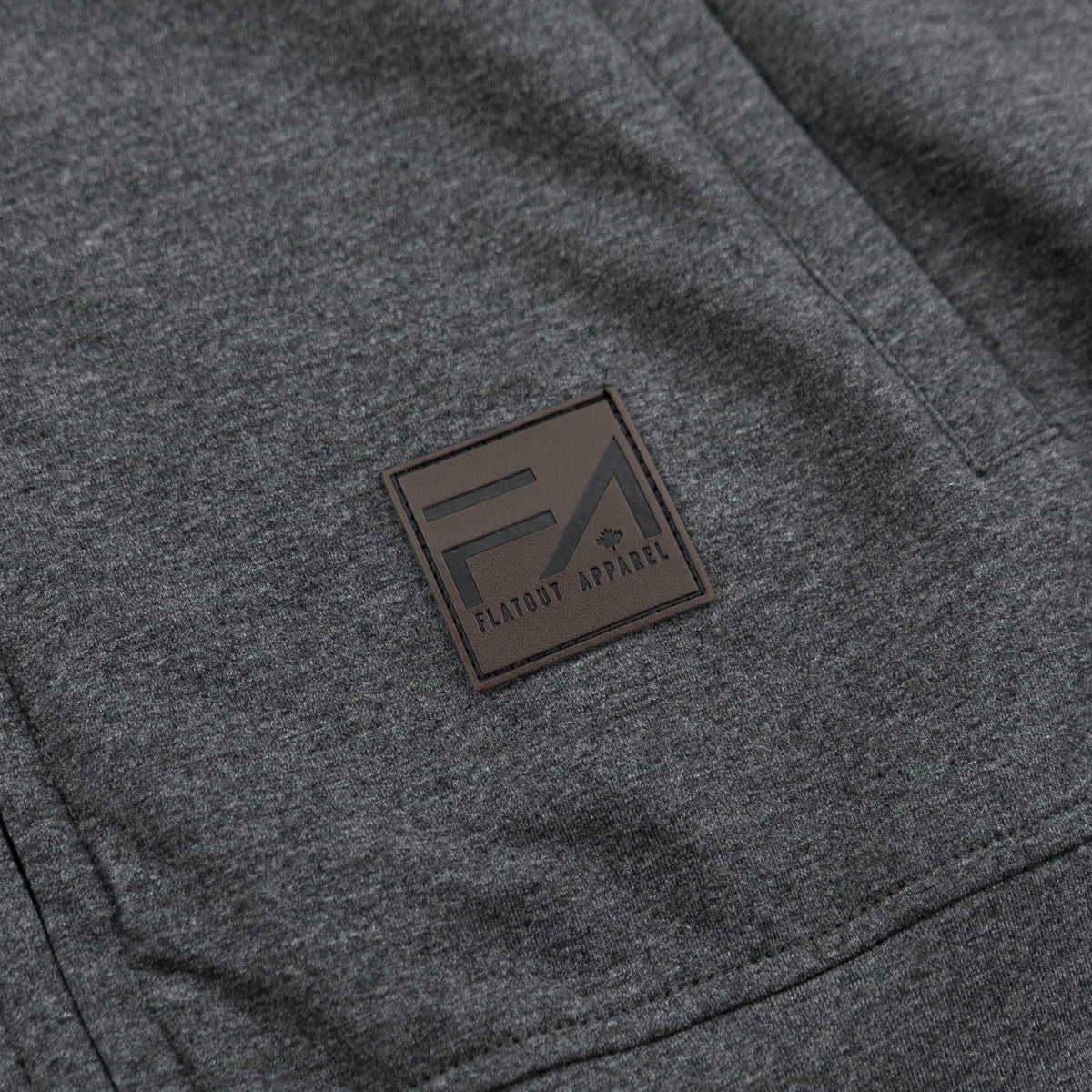 Close-up of a dark heather gray garment with a square brown patch featuring the Flavour Apparel logo.
