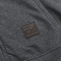 Close-up of a dark heather gray garment with a square brown patch featuring the Flavour Apparel logo.