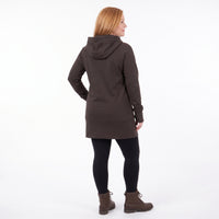 A woman with blonde hair is shown from the back wearing a dark brown hooded tunic sweater, black leggings, and brown boots against a white studio background.