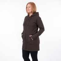 A woman wearing a dark brown zip-up hooded sweatshirt with side pockets, paired with black leggings, standing against a plain white studio background.