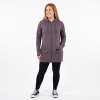 A woman modeling a dusty purple zip-up hoodie with black leggings and black sneakers, standing against a plain white studio background.