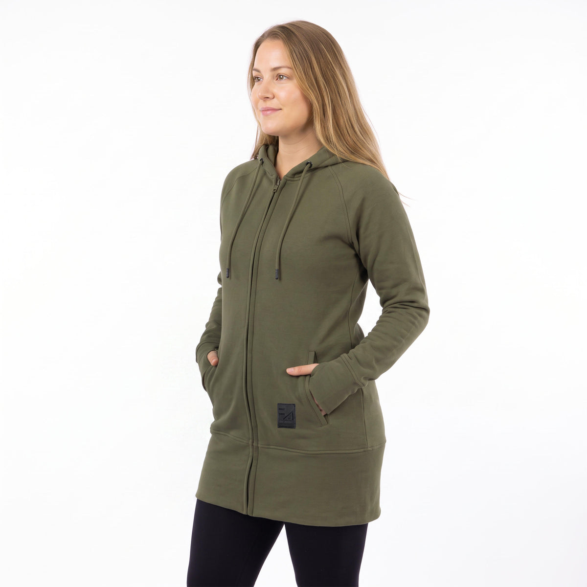 A woman wearing an olive green full-zip hooded sweatshirt with drawstrings and front pockets, standing against a plain white studio background.