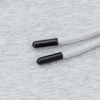 Close-up of white braided drawstrings with black plastic tips embossed with the brand name FLATOUT, laid on a light gray heathered fabric background.