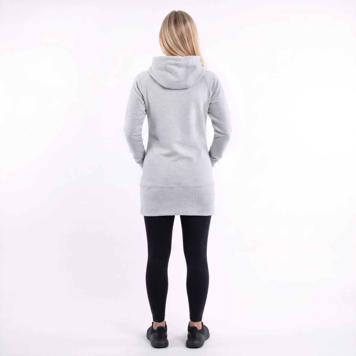 A woman viewed from behind wearing a light gray hooded sweatshirt, black leggings, and black shoes against a plain white studio background.