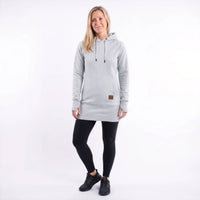 A woman modeling a light gray heathered pullover hoodie with black drawstrings and a small brown brand patch near the hem, paired with black leggings and black sneakers, against a plain white studio background.